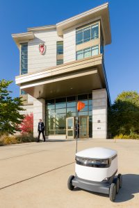 A Starship Delivery robot stands ready to deliver food outside Dejope Residence Hall.